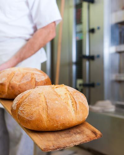 Image of baker removing two artisan loaves from commercial oven