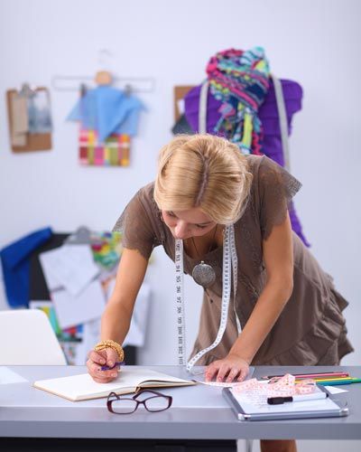 Image of a fashion designer with tape measure around her neck working in a sketch book